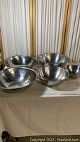 Five stainless steel mixing bowls of varying sizes placed on a table with a cream cloth in front of a light background panel.