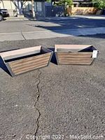 Two rectangular hard plastic garden planters shown outdoors, casting shadows, with visible wood grain texture and light weathering.