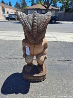 Full view of the carved wooden Hawaiian Polynesian god statue, showing front and headdress detail under outdoor lighting.