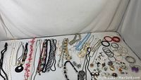 Overview of necklaces, bracelets, and grouped earrings and brooches on a white surface