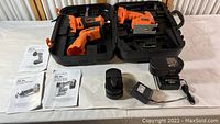 The full set of Proxone cordless tools including detail sander, jigsaw with laser guide, roto tool, two batteries, charger, all inside an open hard plastic carrying case. Manuals placed nearby.