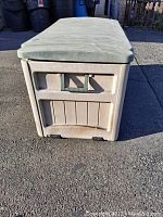 Front angled photo of tan Suncast resin deckbox closed, showing textured lid and side paneling.