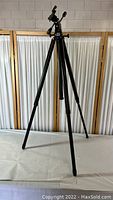 Black folding adjustable tripod standing upright showing full height and adjustable legs.