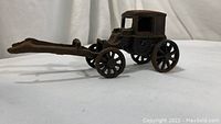 Side angle view of vintage cast iron horse carriage showing the front shafts and spoked wheels with surface rust and wear.