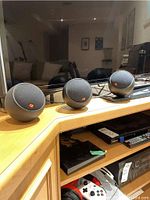 Three small spherical speakers with mesh fronts and red square logos on wooden cabinet