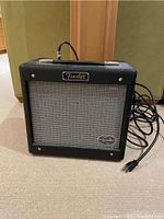 Front view of black Fender G-DEC guitar amplifier with silver speaker grille and attached power cord.