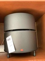 Front view of matte black cylindrical subwoofer on shelf