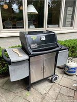 Front view of Weber Genesis Silver barbecue with side tables and propane tanks