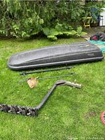 Black Thule cargo box, mounting rails, and hitch bike rack laid on grass