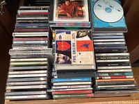 Four stacks of music CDs on shelf showing jewel cases with artists such as Phil Collins, Paula Cole, Michael Jackson and a blank CD-R.