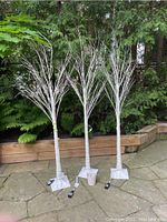 Three assembled white decorative trees standing outdoors on stone paving, showing full height and bases