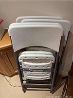 Photo of four folded plastic chairs stacked together, showing the seat and backrest surfaces and metal frame.