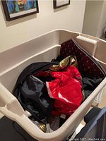Beige plastic tub filled with assorted costume fabric in red, black, gold, and other colors