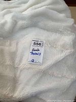 Close-up of white faux fur throw with lot sticker indicating 'plants throws'