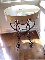 Round metal table with bee motifs on cream painted top and scalloped edge apron, wrought metal black base with gold trim and decorative elements, showing wear and light paint chipping.