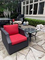 PVC woven patio chair with red cushions beside square glass top patio table