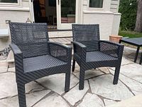 Two black PVC woven chairs on stone patio, view from front left