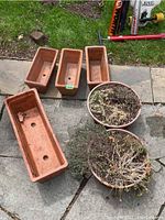 Seven terracotta planters arranged on patio stones, including four rectangular and three circular, with soil residue and dried plants visible.