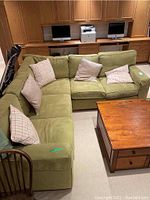 U-shaped arrangement of three green fabric couch segments with five throw pillows, basement setting