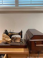 Singer sewing machine next to wooden case on wood surface under window blinds