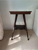 Side view of the antique wooden occasional table showing turned legs and lower decorative shelf