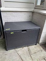 Front view of PVC woven patio trunk against brick wall