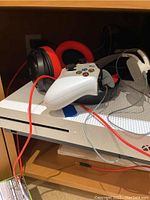 White Xbox One S console with controller on shelf with headsets stacked