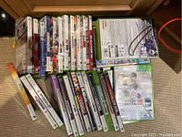 Photo showing 22 Xbox 360 game cases arranged in two rows on carpet with visible titles including NHL 16, Kinect Sports, Call of Duty series, and others.