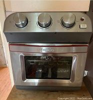 Front view of Dash compact air fryer oven showing control knobs, door handle, and glass window.