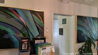 Room view showing two large framed abstract artworks on the wall with vibrant multi-colored curved patterns.