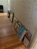 Photo showing multiple framed artworks leaning against a wall, various sizes and styles visible