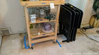 Wooden chef cart with shelves holding various kitchen items and black tray tables stacked beside it