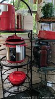 Photo showing red Ninja air fryer, dark brown popcorn popper, red ceramic cookware, and additional red appliance on metal racks