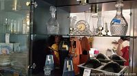 Glass decanters, mantel clock, and glass oil lamps displayed in glass cabinet
