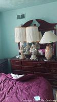 Three ceramic lamps on wooden dresser, two floral with child figures and one marble-effect.