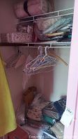View of mostly unopened linens on closet shelves including various boxed and bagged bedding items and hangers