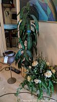 Photo showing tall faux plant, faux floral arrangement with cream-colored flowers, metal plant stand with dark pots