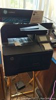 Front view of HP LaserJet printer showing touchscreen, automatic document feeder, paper output tray, and power cord.