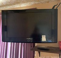 Samsung 31-inch TV mounted on wall with remote on shelf beneath it, showing front of TV and visible cables.