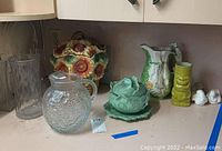 Various glass and ceramic pitchers, sunflower ceramic cookie jar, cauliflower serving dish with lid, vases and small figurines on countertop