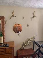 Seven wall decorations with bird designs arranged on a wall. Includes a large round copper-toned piece with flying birds and six separate metal bird figures around it.