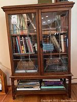 Full front view of cabinet showing two leaded glass pane doors, interior shelves stocked with books and lower open shelf.