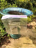 Green-blue patina metal birdbath shown on stone path with water and leaves inside basin