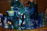 Wide view of blue glassware collection arranged on mirrored surface showing variety of pitchers, bowls, jugs, vases, and decorative pieces.