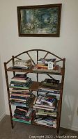 Full front view of the wooden bamboo-style book shelf filled with miscellaneous books and a framed picture hanging above it.