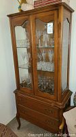 Front view of vintage wooden china cabinet showing glass doors and interior glass shelves with some glassware inside.