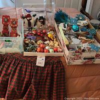 Overview photo showing plaid tablecloth and multiple trays of Christmas decorations on bed