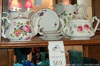 Full shelf view showing floral patterned teapot, pitcher, and matching saucer plates with other dishes.