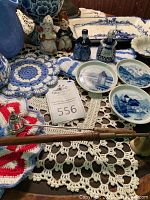 Wide view showing porcelain figurines, small plates with blue scenic patterns, brass candle snuffer and crocheted doilies.
