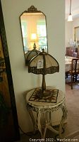Overall view of side table topped with slag glass lamp, positioned in front of wall mirror